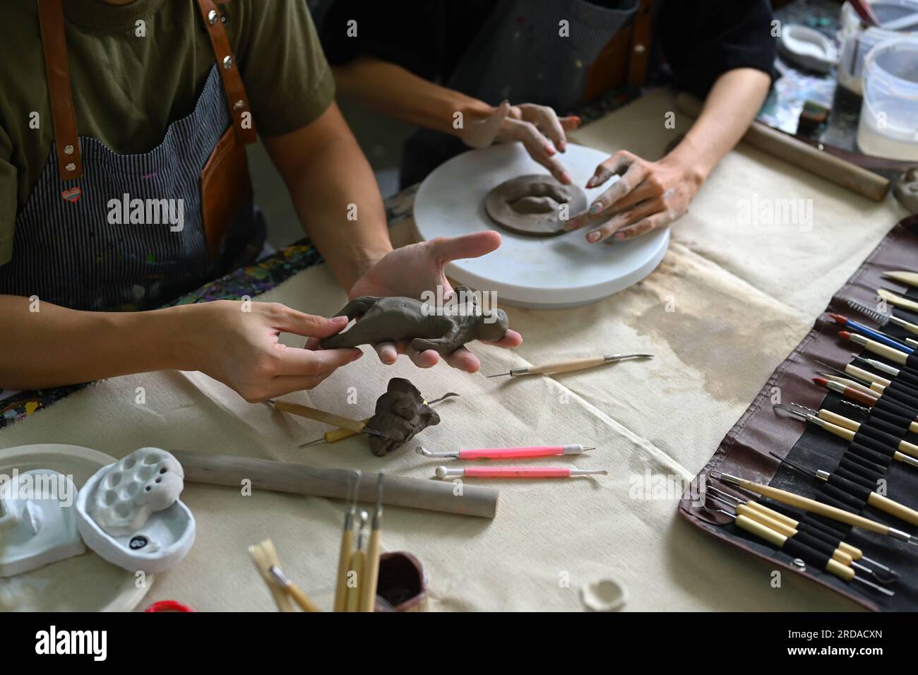 Craftspeople wearing aprons working with raw clay, shaping and decorating pottery in workshop Stock Photo