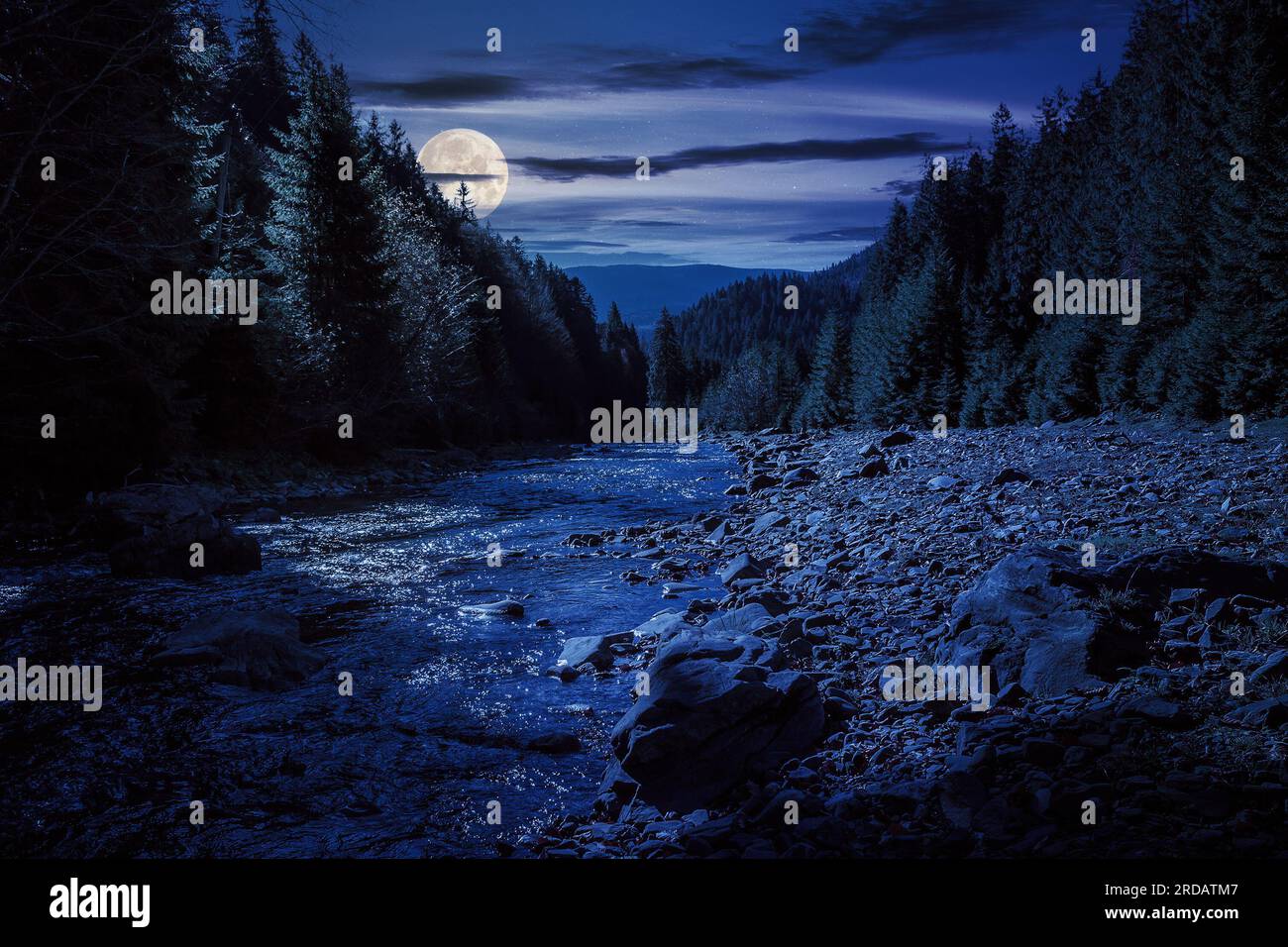 autumn landscape at night. rocky shore of the river that flows near the pine forest at the foot of the mountain in full moon light Stock Photo