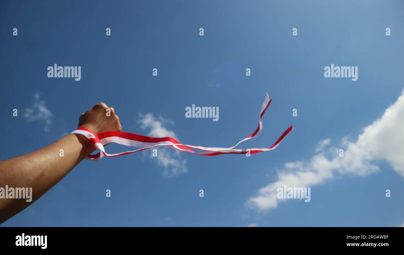 Hand wearing red and white ribbon with blue sky background, Indonesia independence day concept Stock Photo