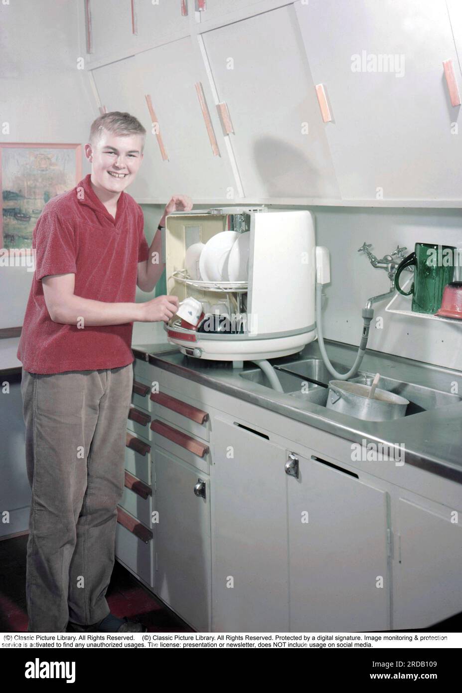 Kitchen in the past. A young man at the Swedish company Electrolux's first dishwasher, the bench dishwasher D10, called the Round jar or round can, which began production in 1959, and then cost SEK 410 plus VAT. The dishwasher was in production until 1973 and was produced in 50,000 copies. The big difference to modern dishwashers was that the string baskets with the dirty plates and glasses rotated inside and was washed clean by stationary jets of water. Sweden 1959. Conard Stock Photo