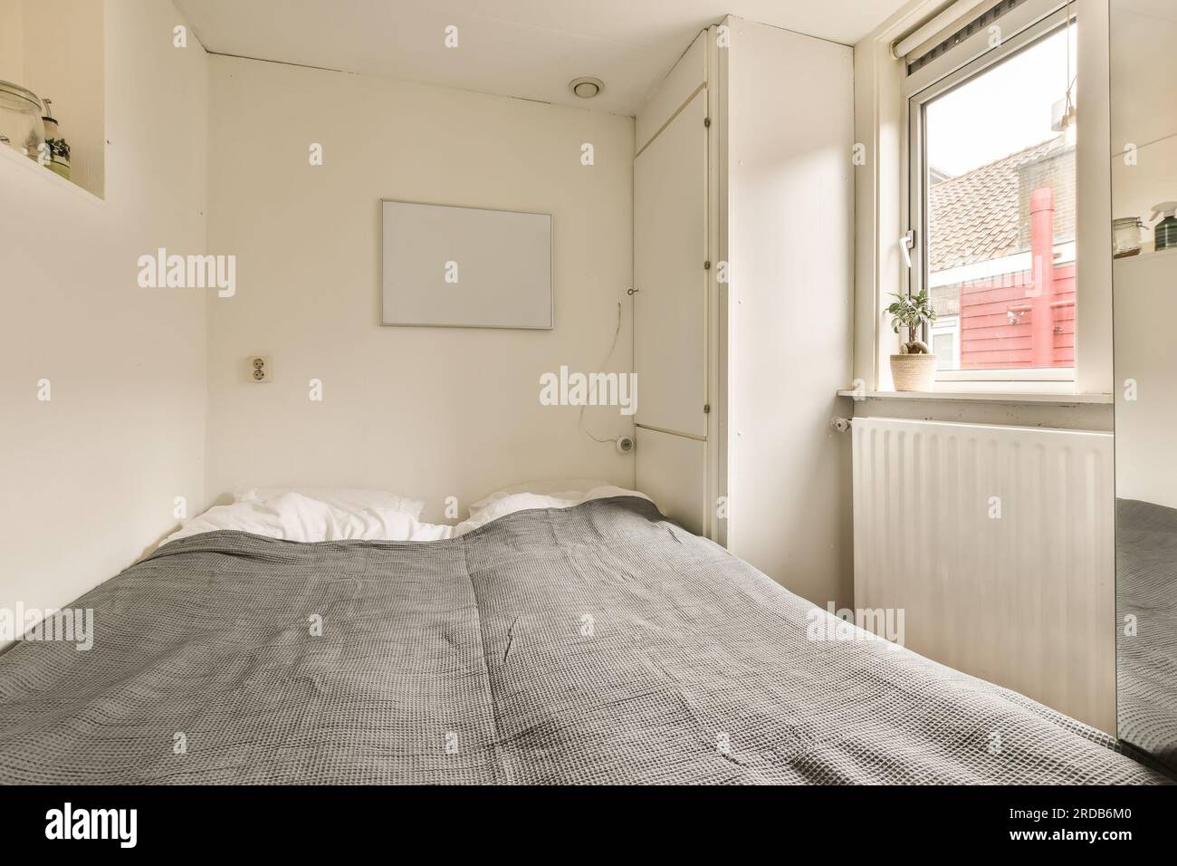 a bed in a room with a window and air conditions on the wall next to the bed  is an electric heater Stock Photo - Alamy
