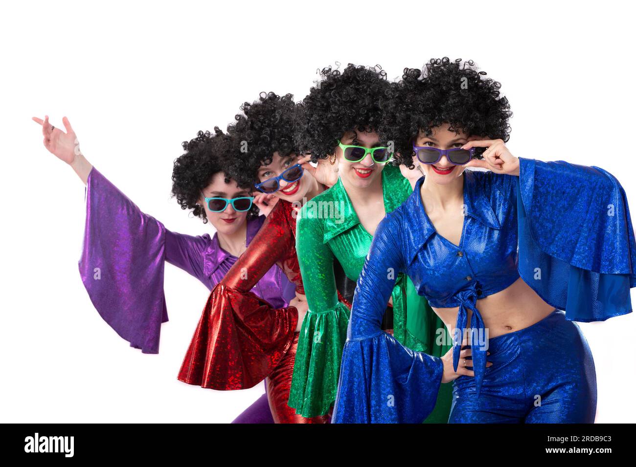 A group of girls in colorful flared suits and afro wigs pose against a white background. Disco style from the eighties or seventies. Stock Photo