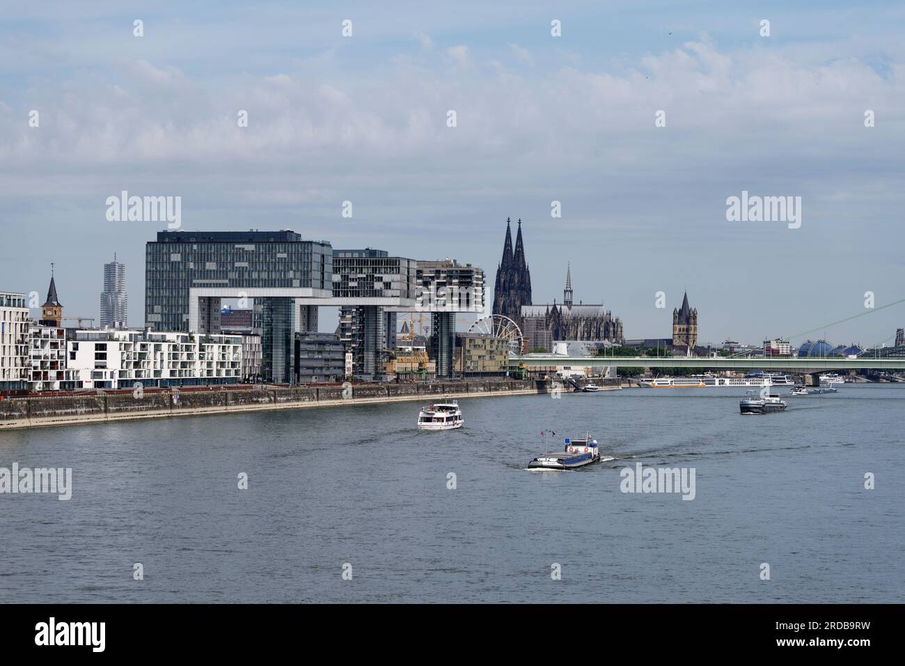 Cologne, Germany July 18 2023: excursion and cargo ships on the rhine in front of the impressive panorama of cologne with the crane houses and the cat Stock Photo