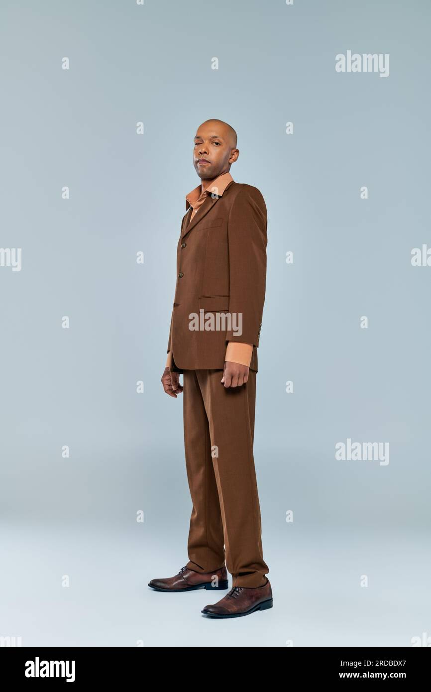 eye syndrome, bold african american man with myasthenia gravis standing on grey background, dark skinned person in formal wear, diversity and inclusio Stock Photo