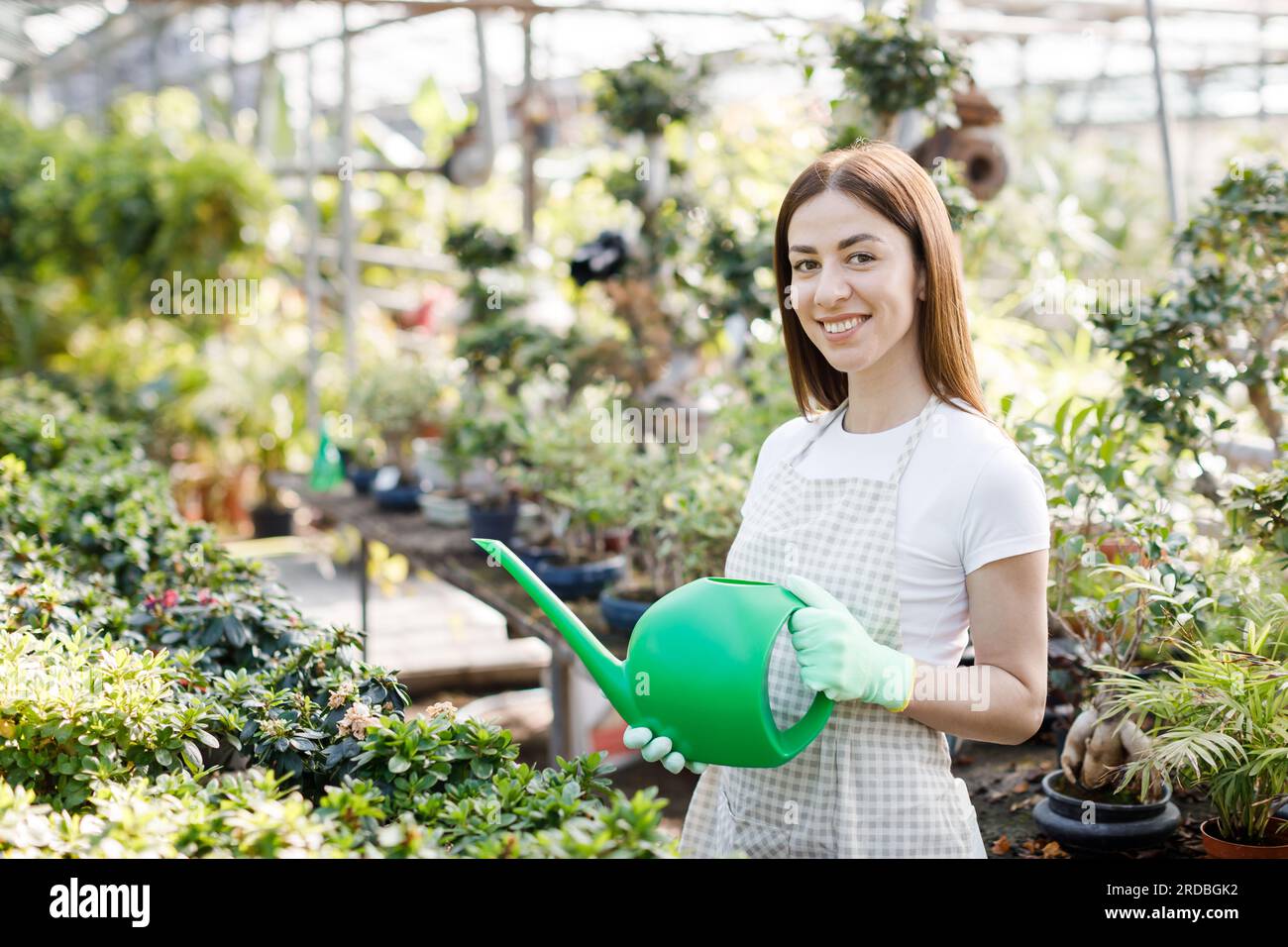 A young woman stands in the middle of a large greenhouse holding a ...
