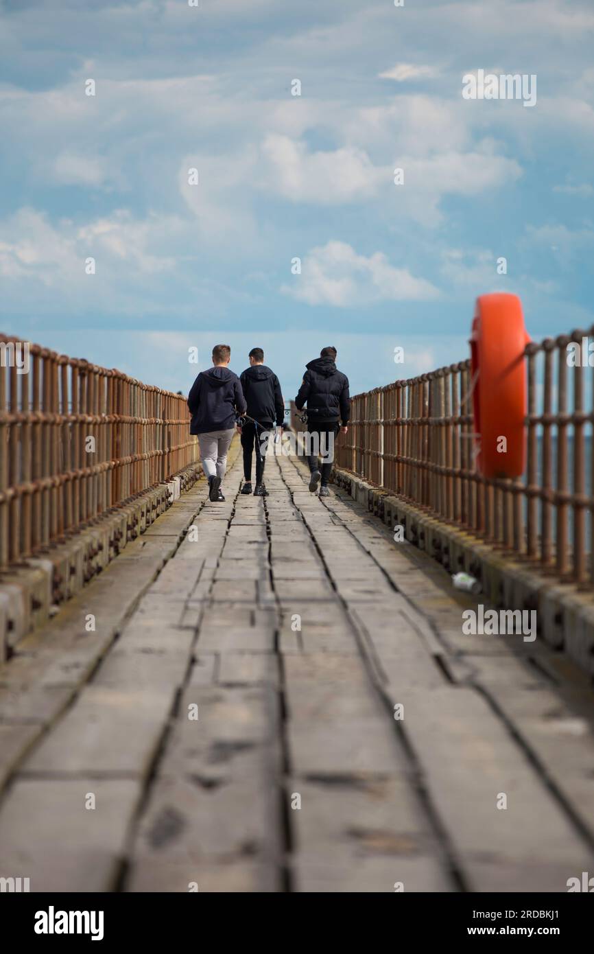 3 boys going fishing walking along Blyth Pier Stock Photo