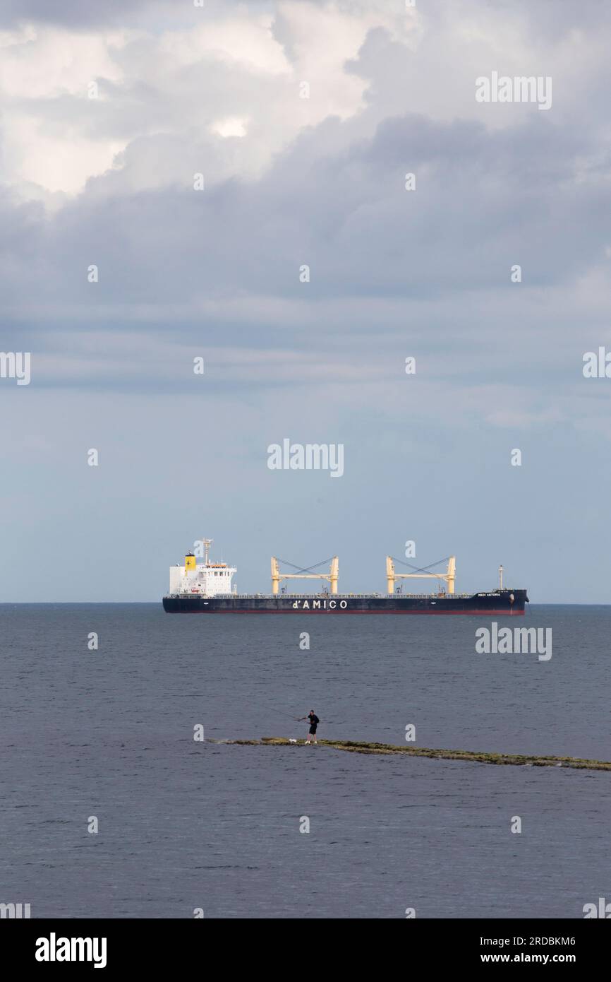 Lone man sea fishing out at sea with large ship in background near Whitley Bay Stock Photo