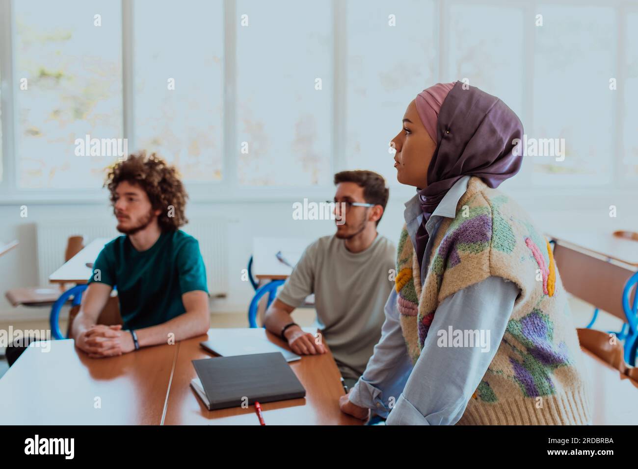 A diverse group of students gathers in a modern school classroom ...