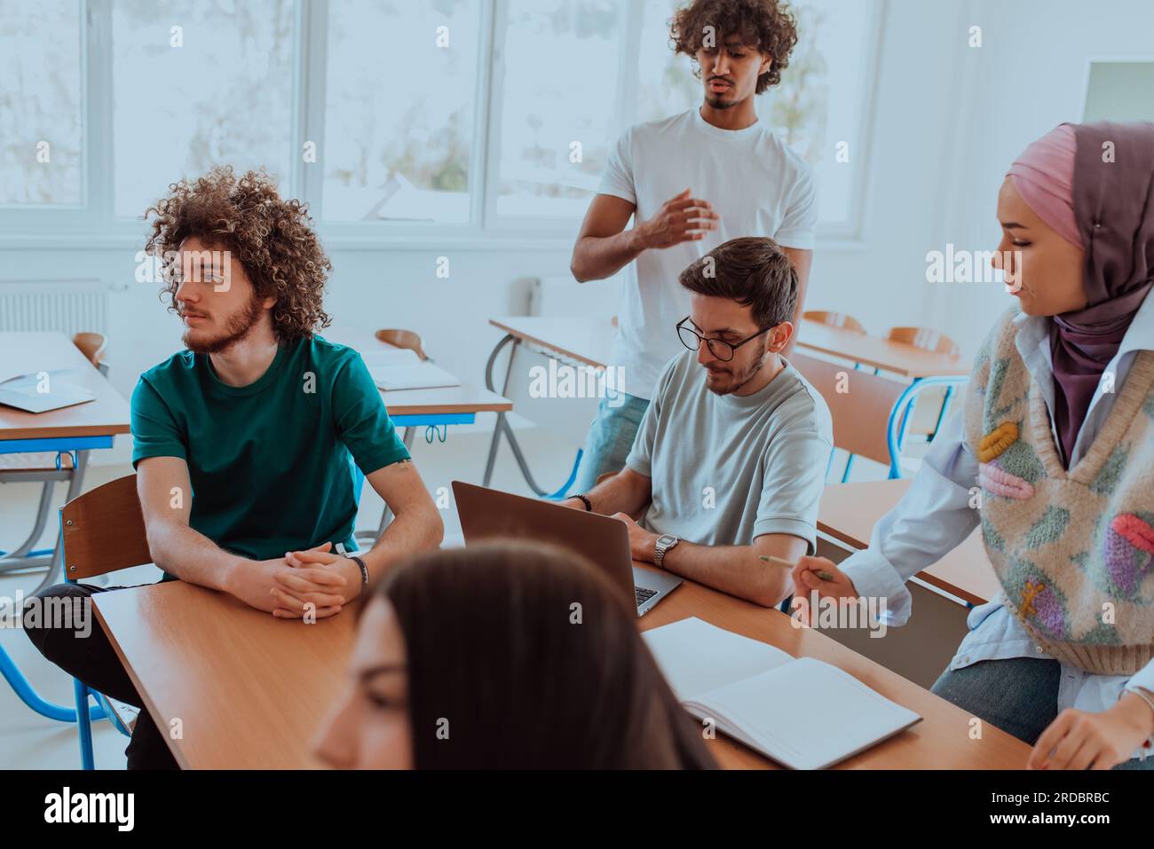 A diverse group of students gathers in a modern school classroom ...