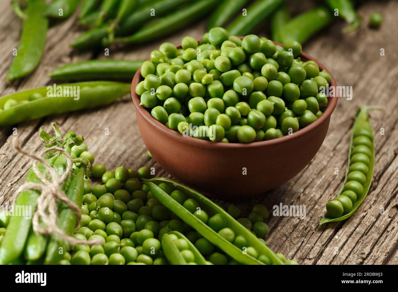 Fresh organic green peas in closed and open pods, scattered pea seeds, shelled green peas in a clay bowl on an aged wooden background. Stock Photo