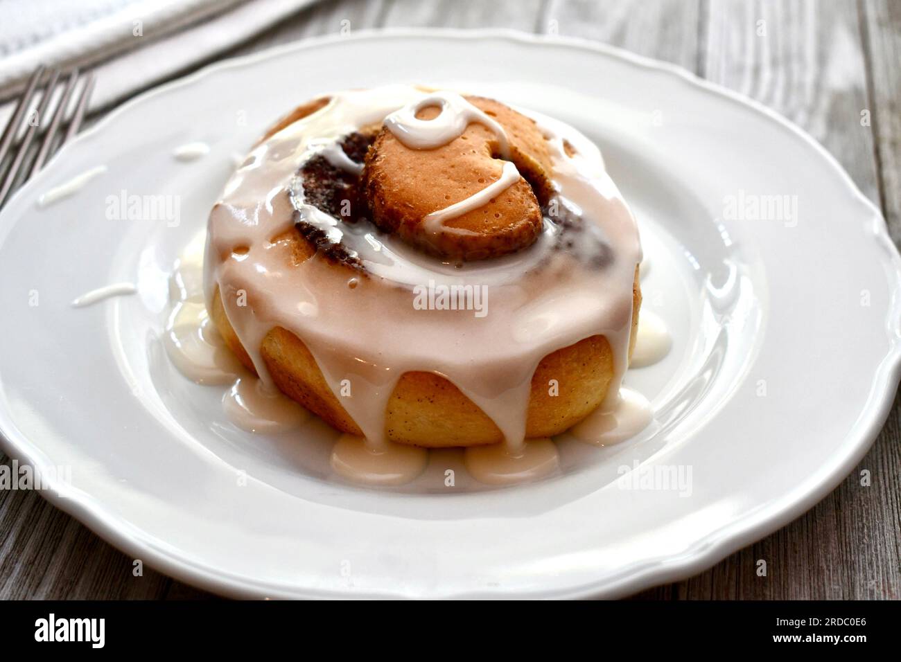 Cinnamon roll drizzled with icing on a white plate Stock Photo