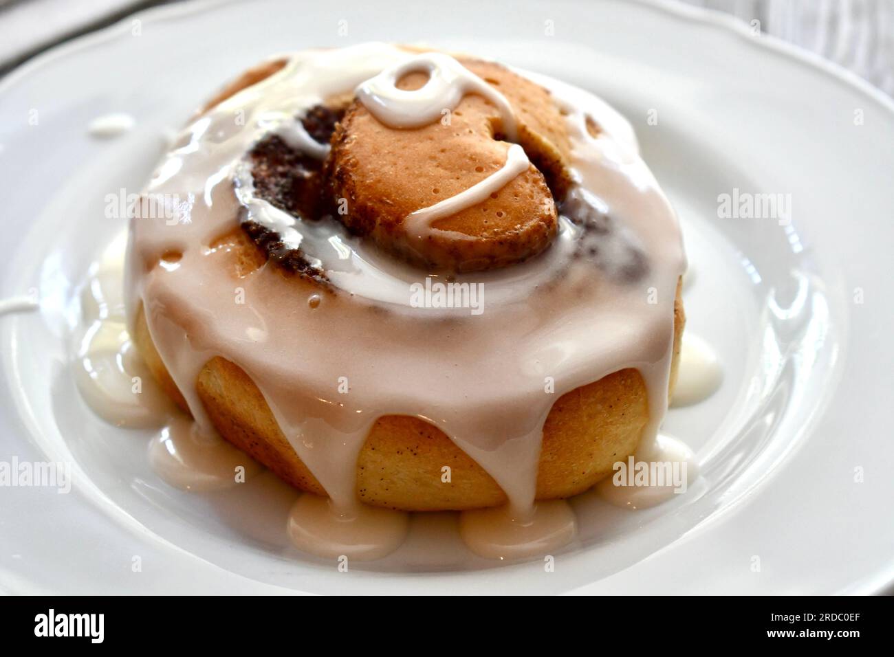 Cinnamon roll drizzled with icing on a white plate Stock Photo