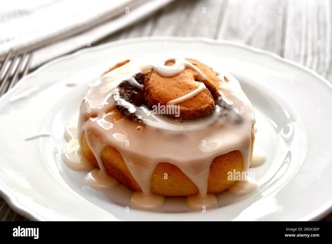 Cinnamon roll drizzled with icing on a white plate Stock Photo