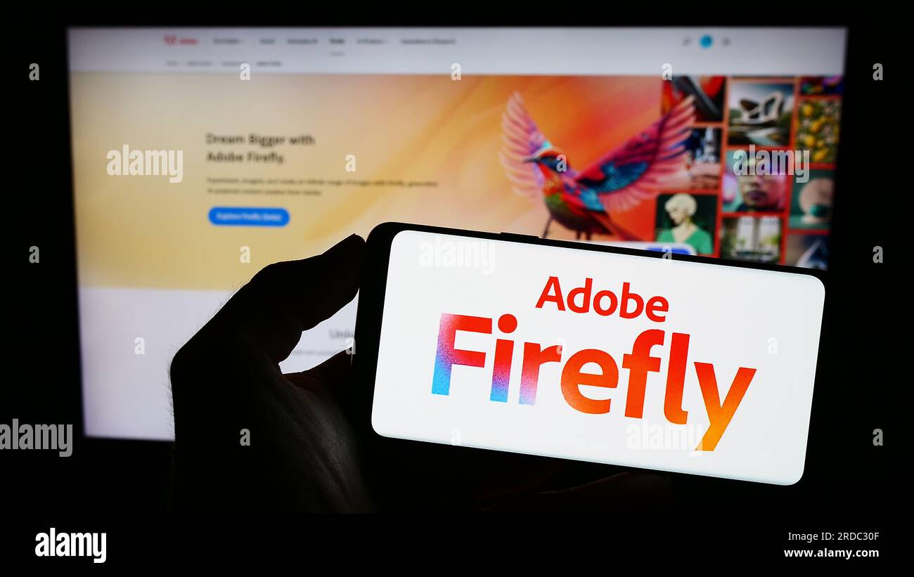 Person holding smartphone with logo of generative AI product Adobe Firefly on screen in front of website. Focus on phone display. Stock Photo