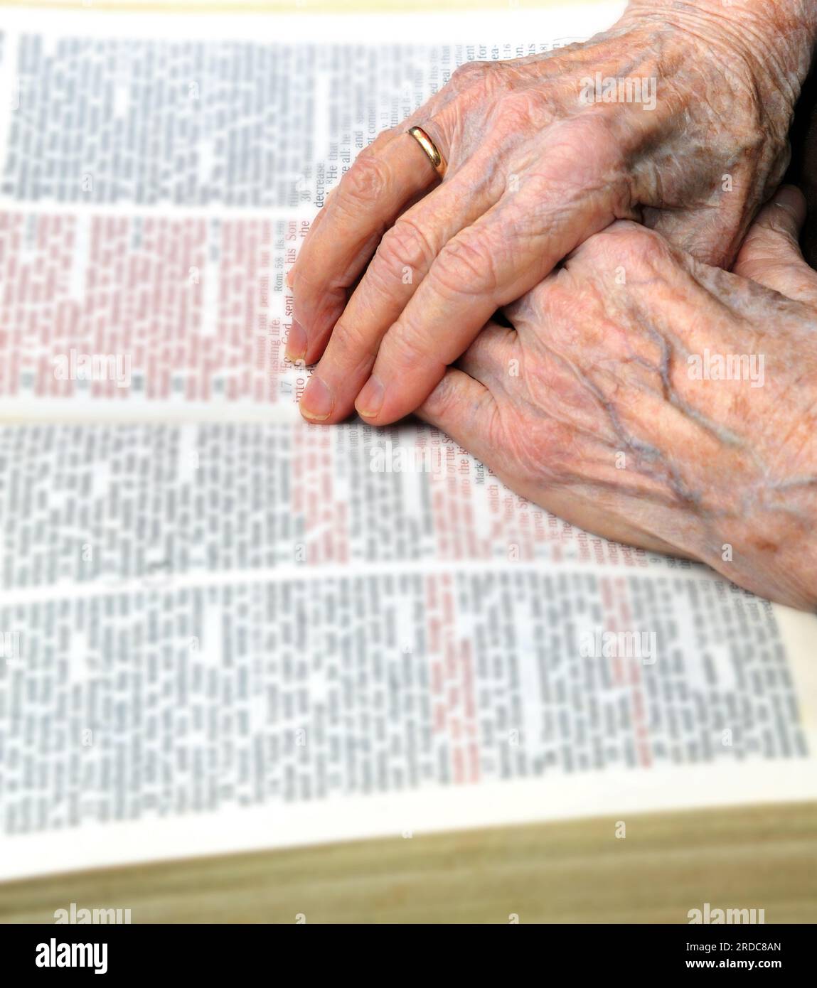 Elderly woman rests her hands on her Bible.  Gnarled and wrinkled hands settle besides John 3:16. Stock Photo