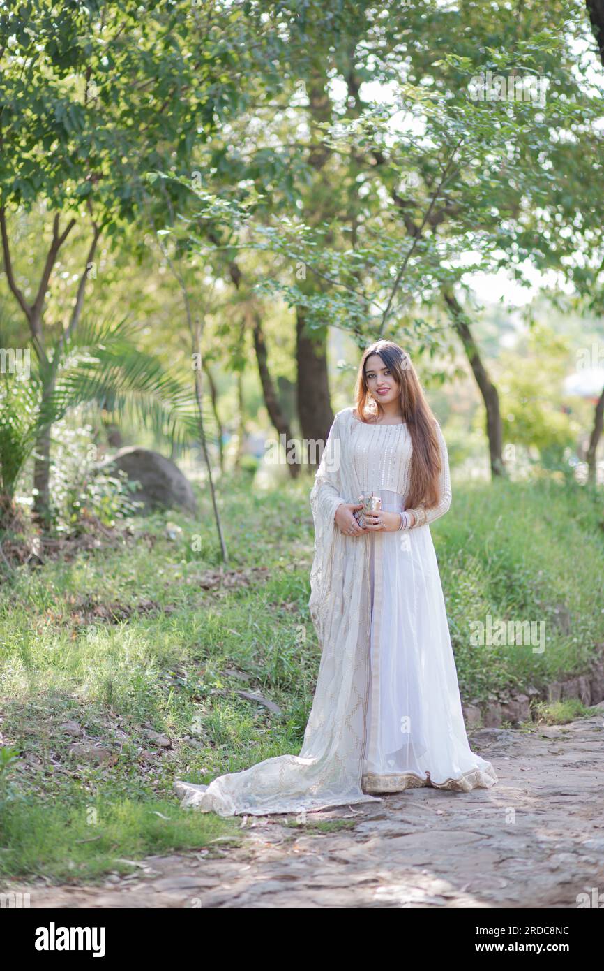 Beautiful Asian Girl posing in front of trees and giving pose. The tummy of girl is revealing and wearing white eastern gown dress Stock Photo