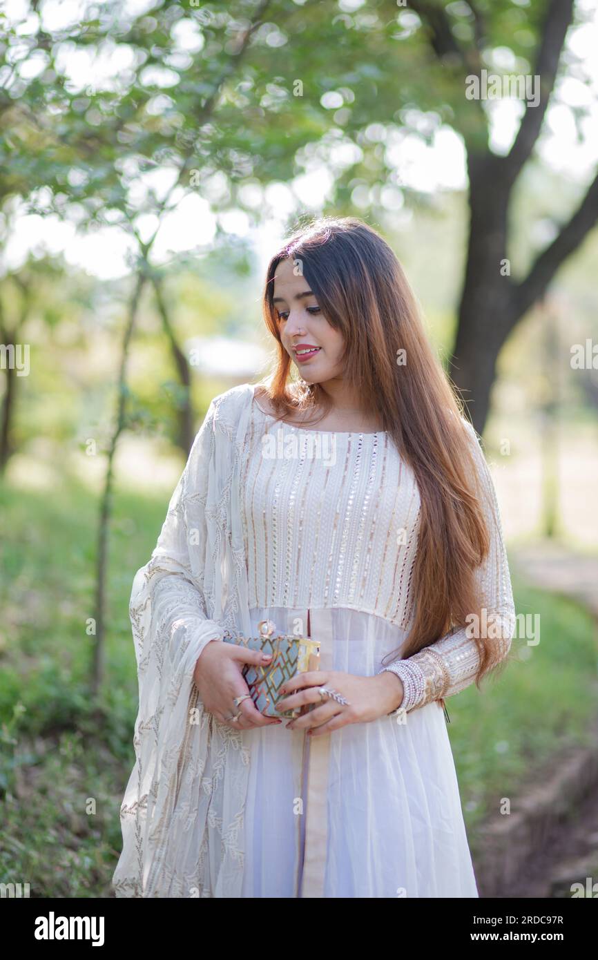 Beautiful Asian Girl posing in front of trees and giving pose. The tummy of girl is revealing and wearing white eastern gown dress Stock Photo