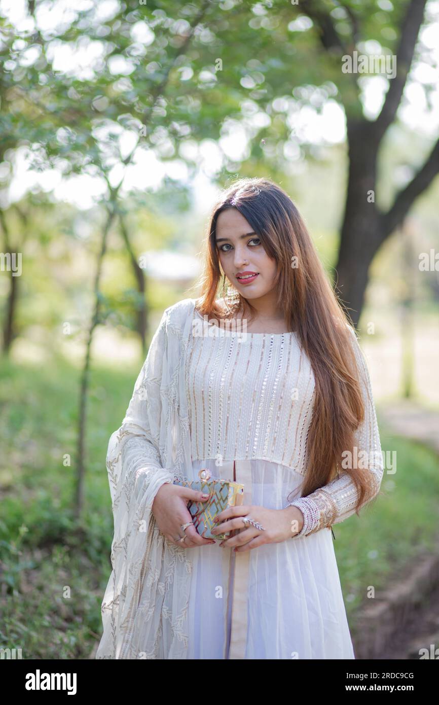 Beautiful Asian Girl posing in front of trees and giving pose. The tummy of girl is revealing and wearing white eastern gown dress Stock Photo