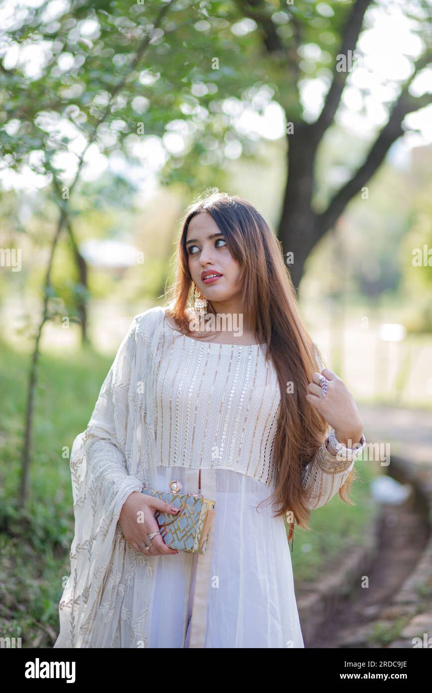 Beautiful Asian Girl posing in front of trees and giving pose. The tummy of girl is revealing and wearing white eastern gown dress Stock Photo