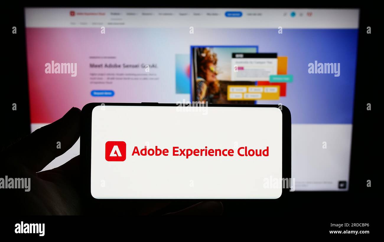 Person holding smartphone with logo of software product Adobe Experience Cloud (AEC) on screen in front of website. Focus on phone display. Stock Photo