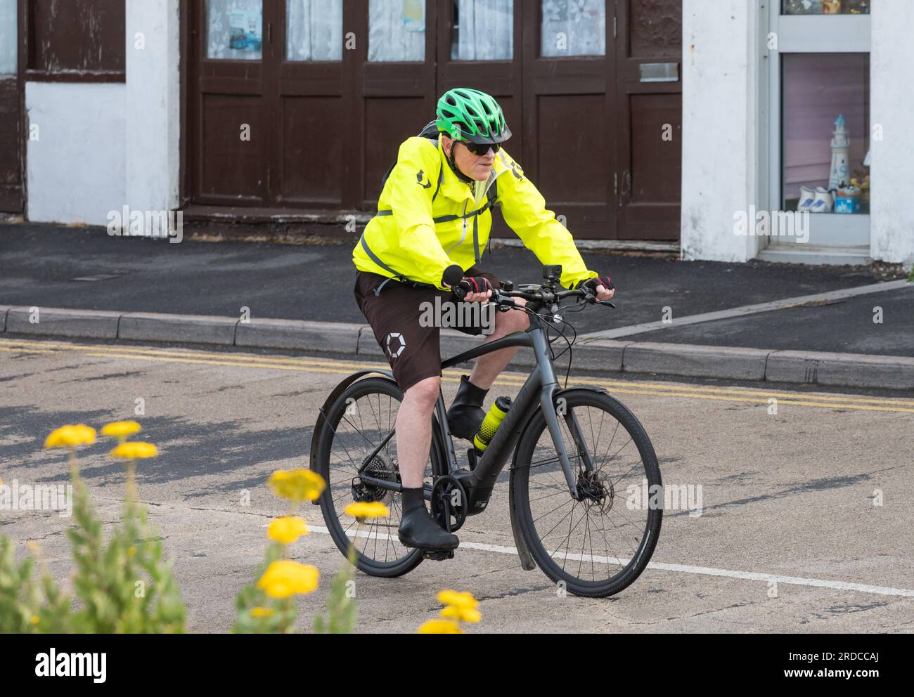 Side view of a male cyclist wearing cycle helmet and hi visibility top riding a bicycle along a road in the UK. Man cycling with hi-vis gear. Stock Photo