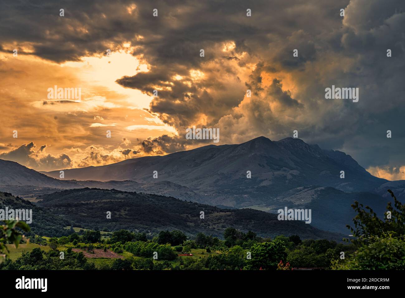 Landscape of the Sirente-Velino mountain range under a stormy sky with clouds illuminated by the red light of the sunset.Sirente Velino Nature Reserve Stock Photo