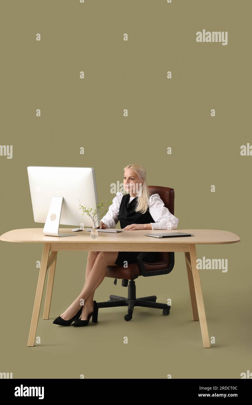 Mature female programmer working with computer at table on green ...