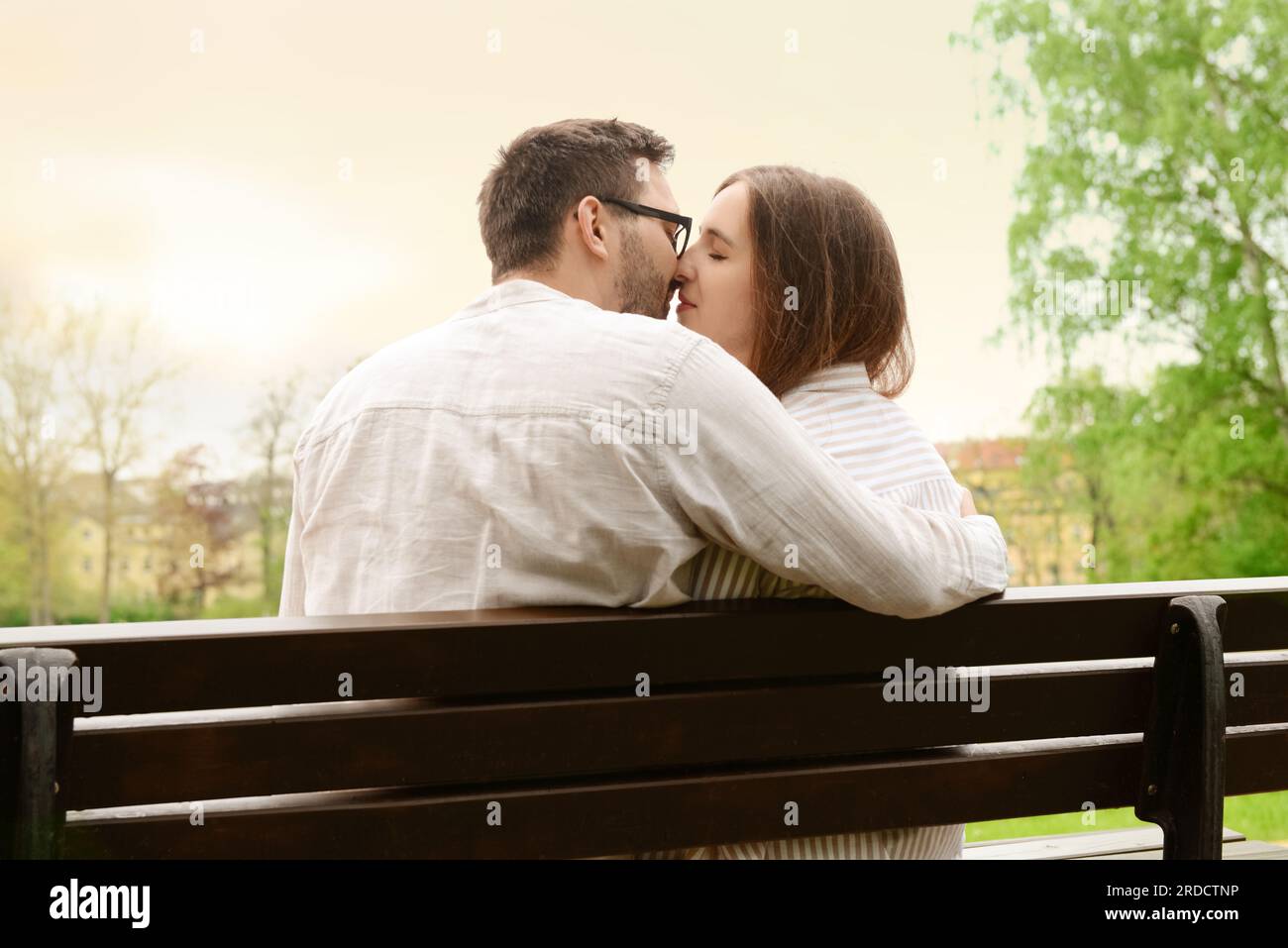 Beautiful loving couple sitting on bench and kissing in park Stock ...