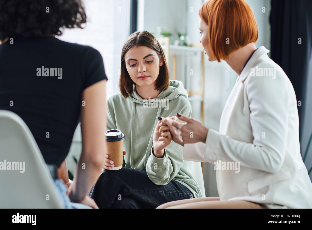 redhead psychologist holding hand of young and sad woman sitting with ...