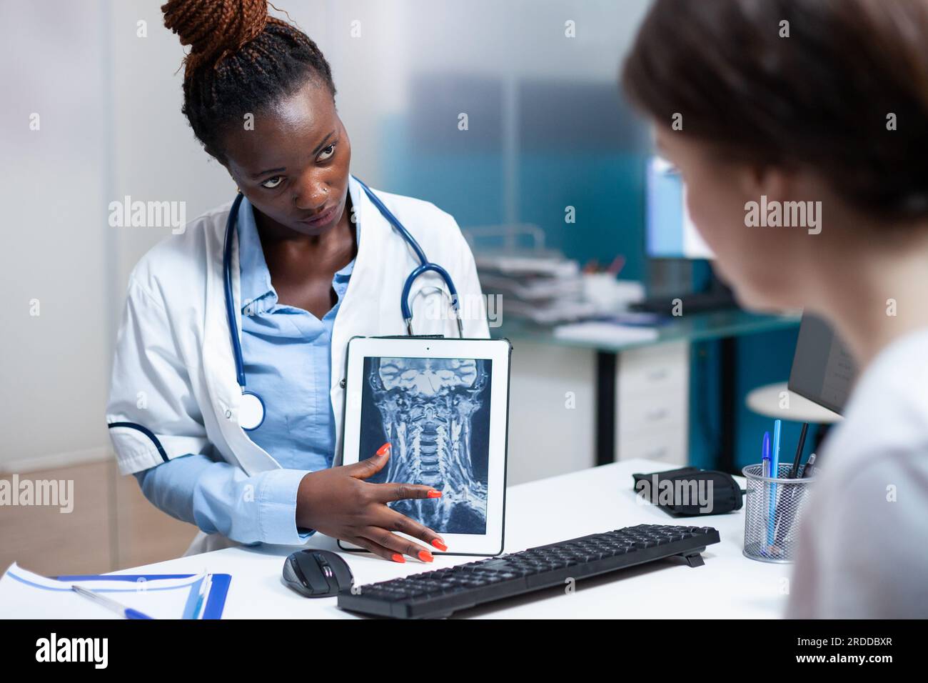 Specialist doctor delivering tomography medical exam results to patient in clinic office. Healthcare specialist showing radiography x-ray ct scan of cervical bone injury on tablet during check-up Stock Photo