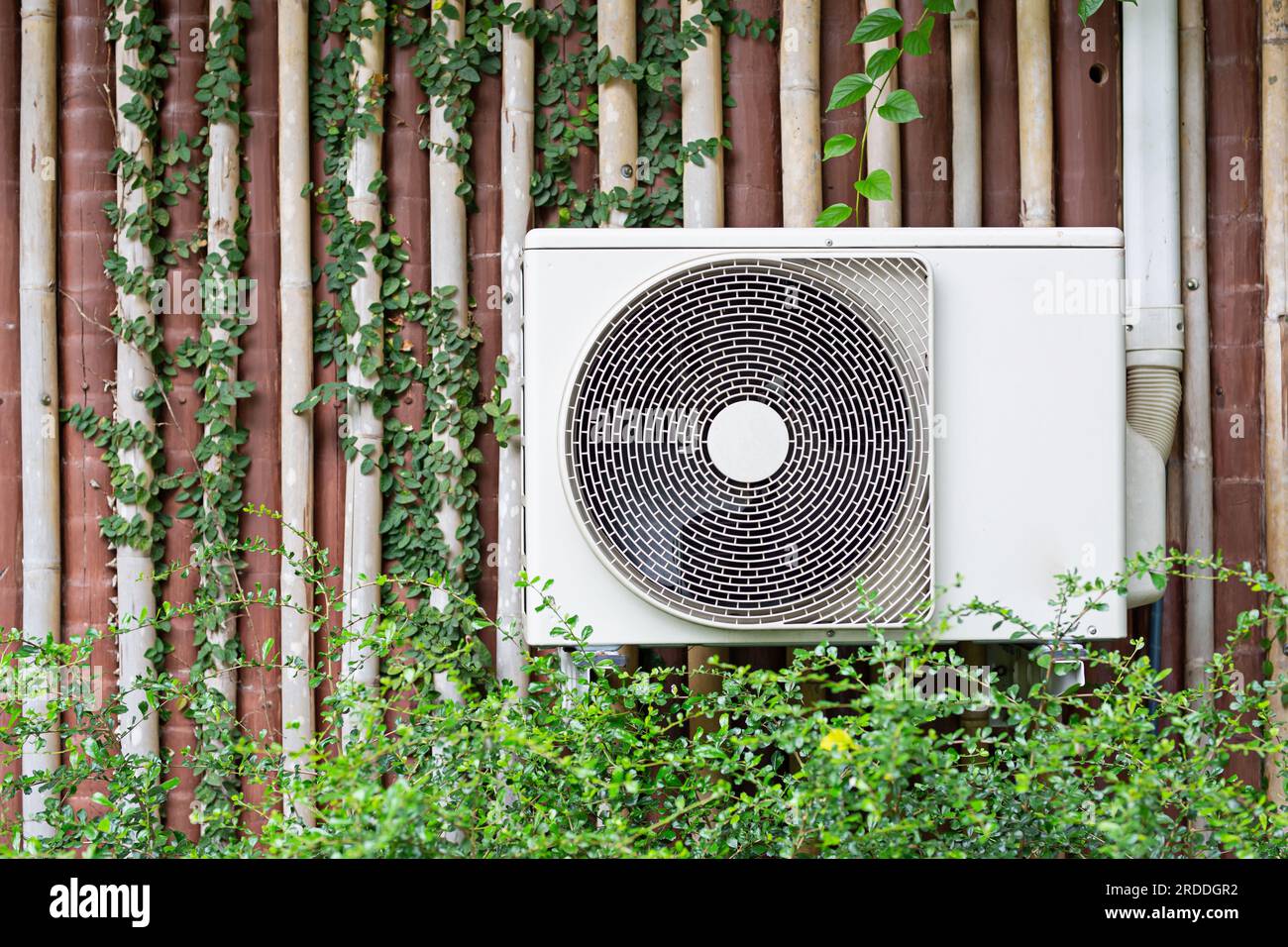 The air conditioner is mounted on the wall with the trees of the building with the garden in the front row. Stock Photo