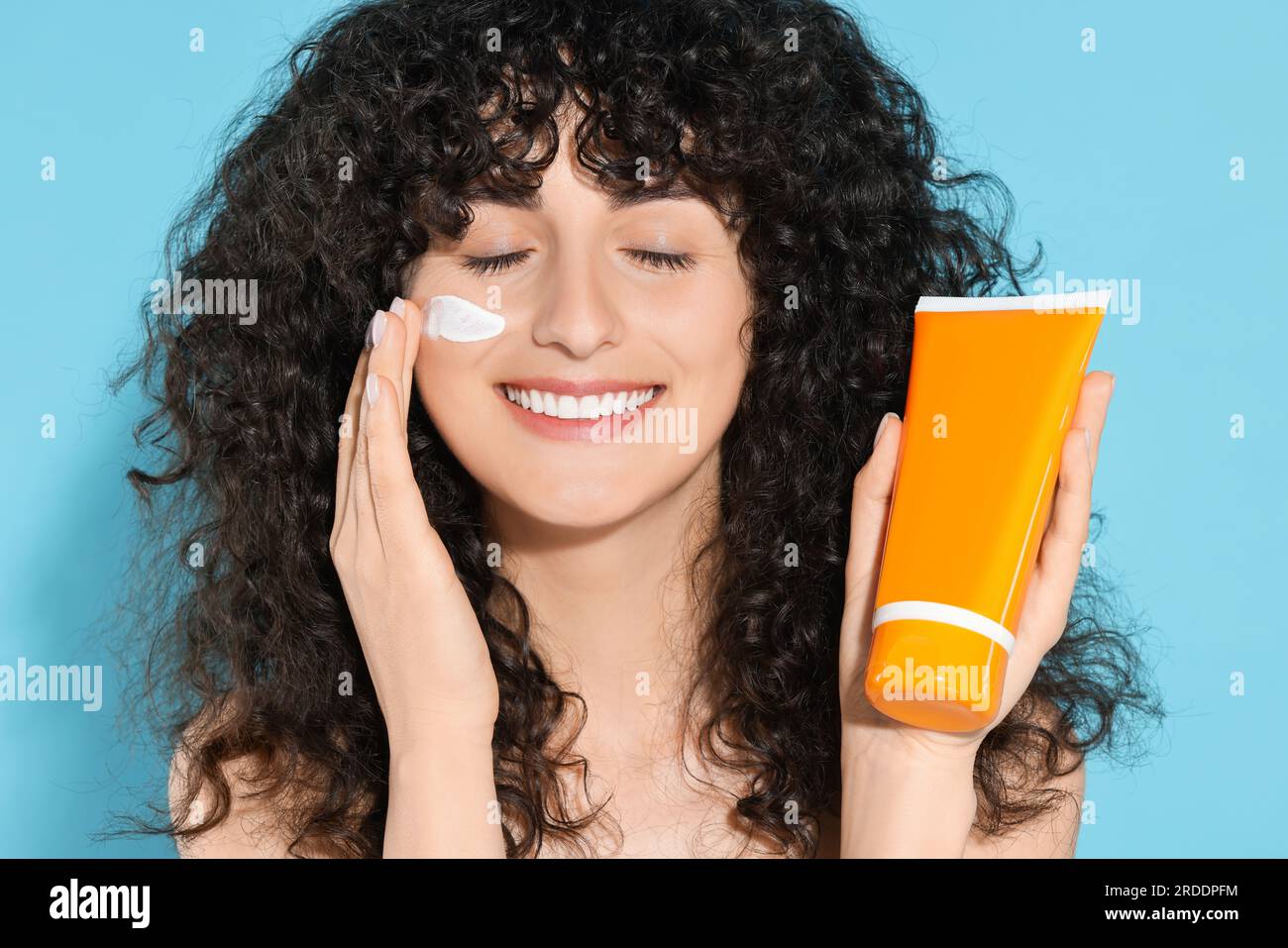 Beautiful young woman with tube of sunscreen applying sun protection ...
