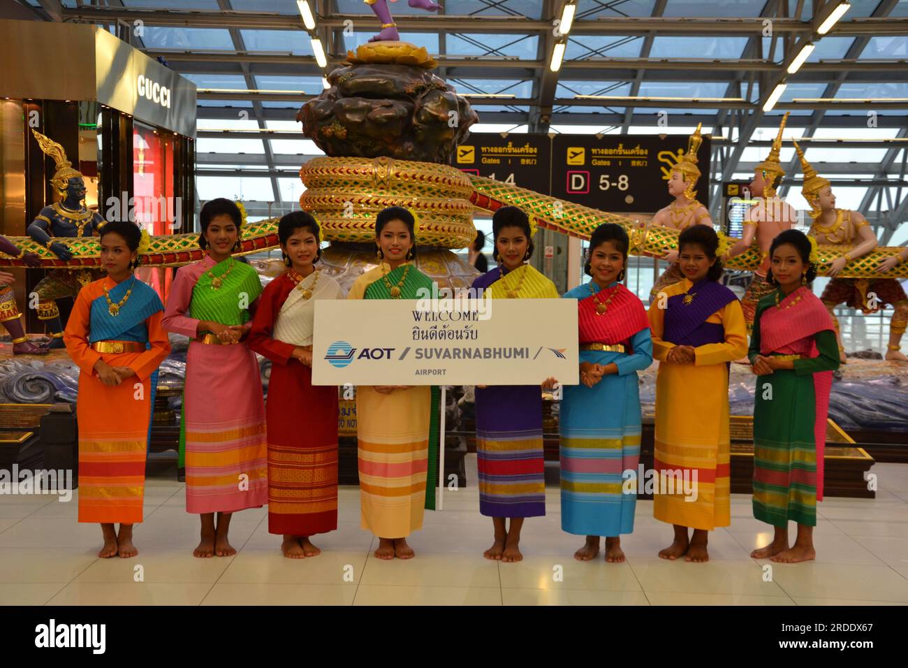 A group of women wearing traditional Thai clothes, holding a message from Airports of Thailand Public Company Limited (AOT), welcome visitors to the departure level, just past immigration checks, Suvarnabhumi International Airport, Bangkok, Thailand, Asia, 2014 Stock Photo