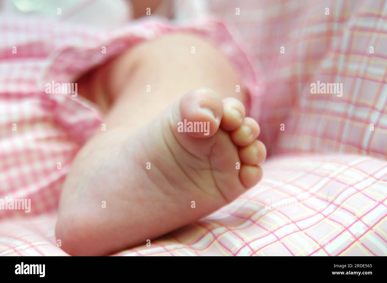 Tiny foot of a newborn baby girl curls toes downward. She is dressed in