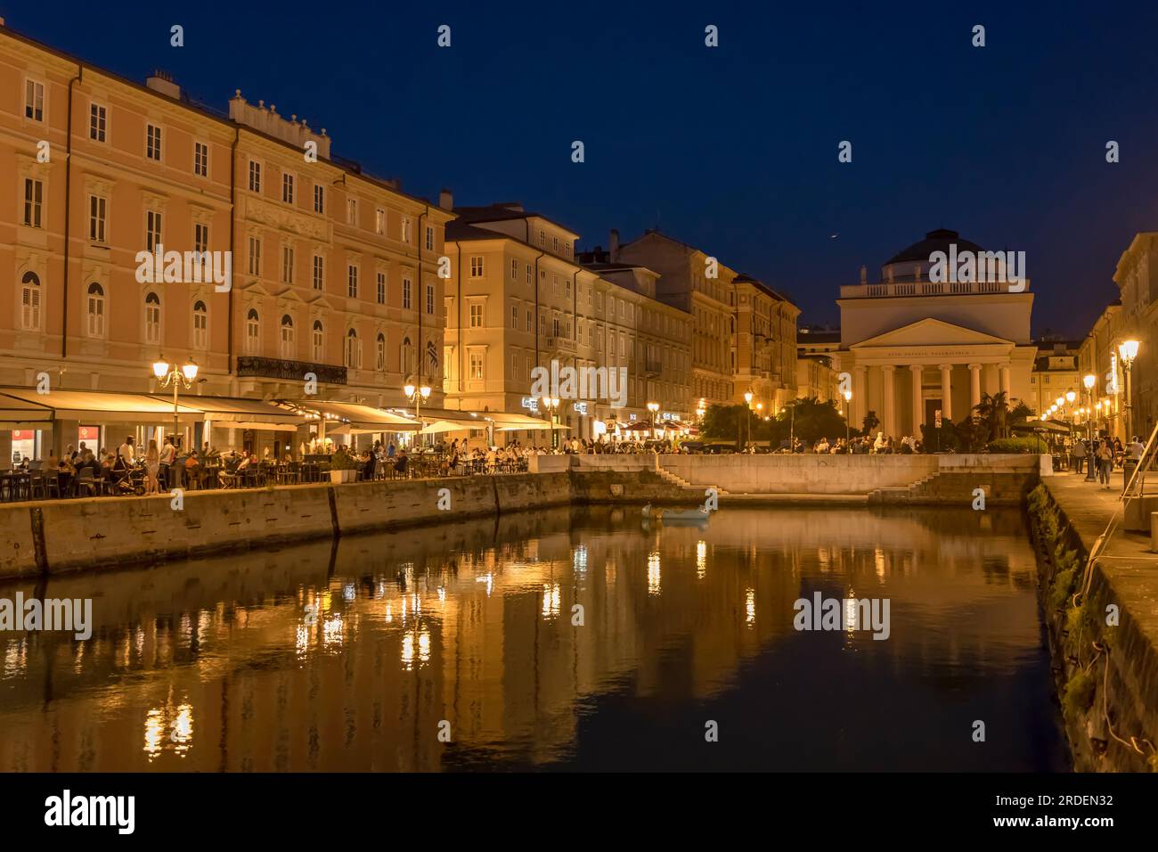 TRIESTE, ITALY - may 29 2023: cityscape with people enjoying evening time on embankment at Canal Grande near Clasical sant Antonio church, shot in nig Stock Photo