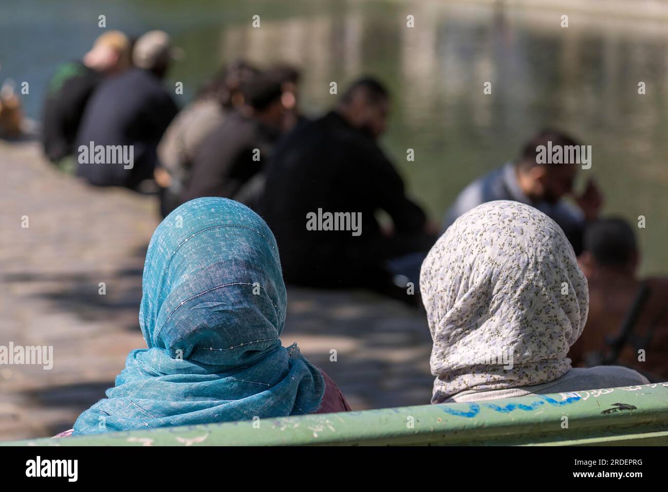 Two woman with headscarves sit on a bench, the men at the back by the old canal, Paris, France Stock Photo