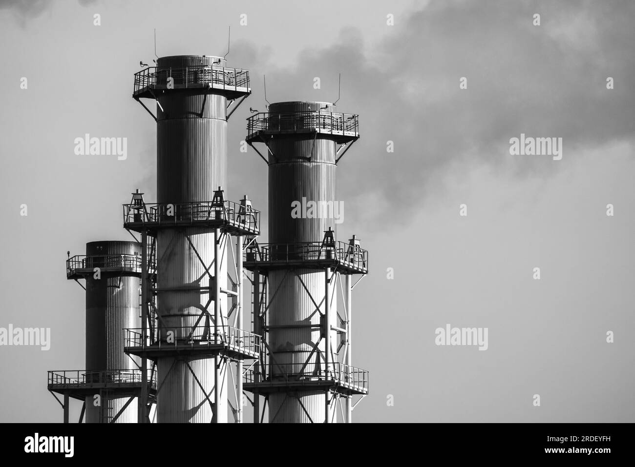 Smoking chimneys are under gray sky on a daytime. Power plant exhaust equipment, black and white photo Stock Photo