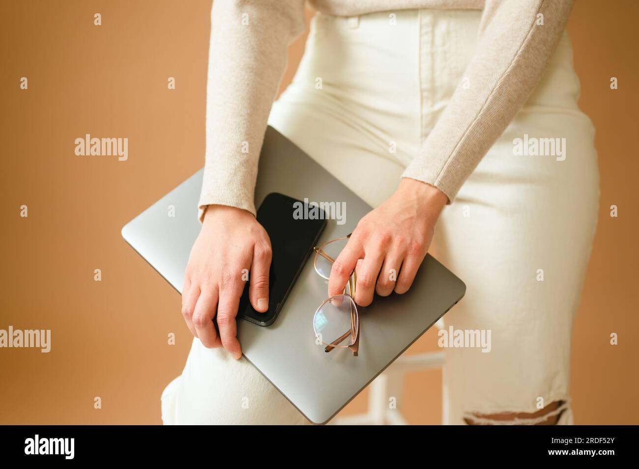 Close up of woman holding smart phone, laptop and glasses on leg Stock Photo