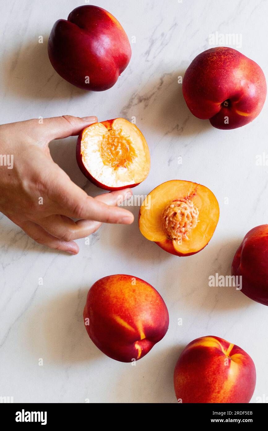 A hand reaching out to grab a ripe nectarine that is cut in half Stock