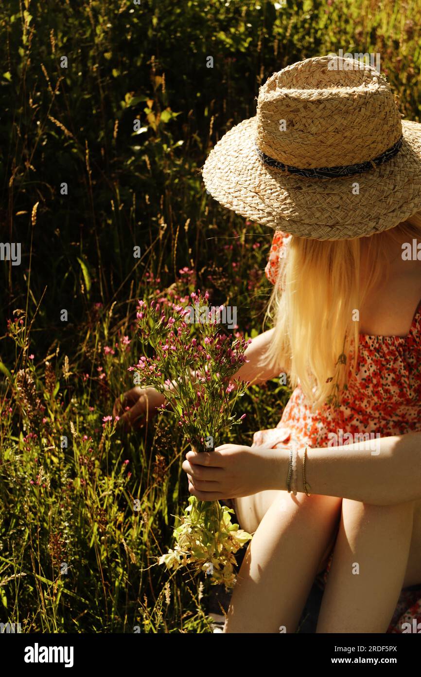 Portrait of a young blonde woman wearing a straw hat with wildflowers ...