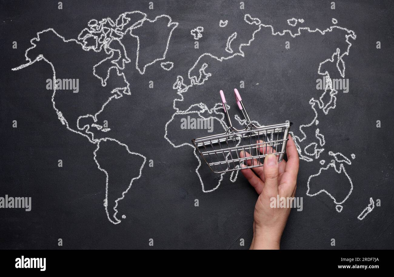 A female hand holding a miniature empty shopping basket against the background of a drawn world map. Concept of online shopping, international shippin Stock Photo