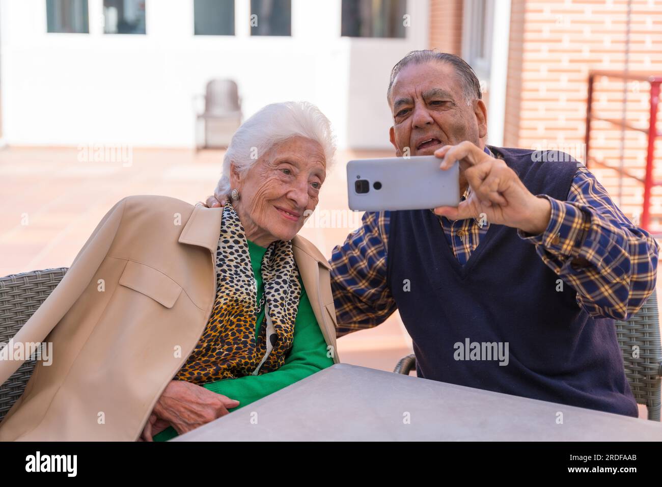Two very happy elderly people in the garden of a nursing home, looking at the phone Stock Photo