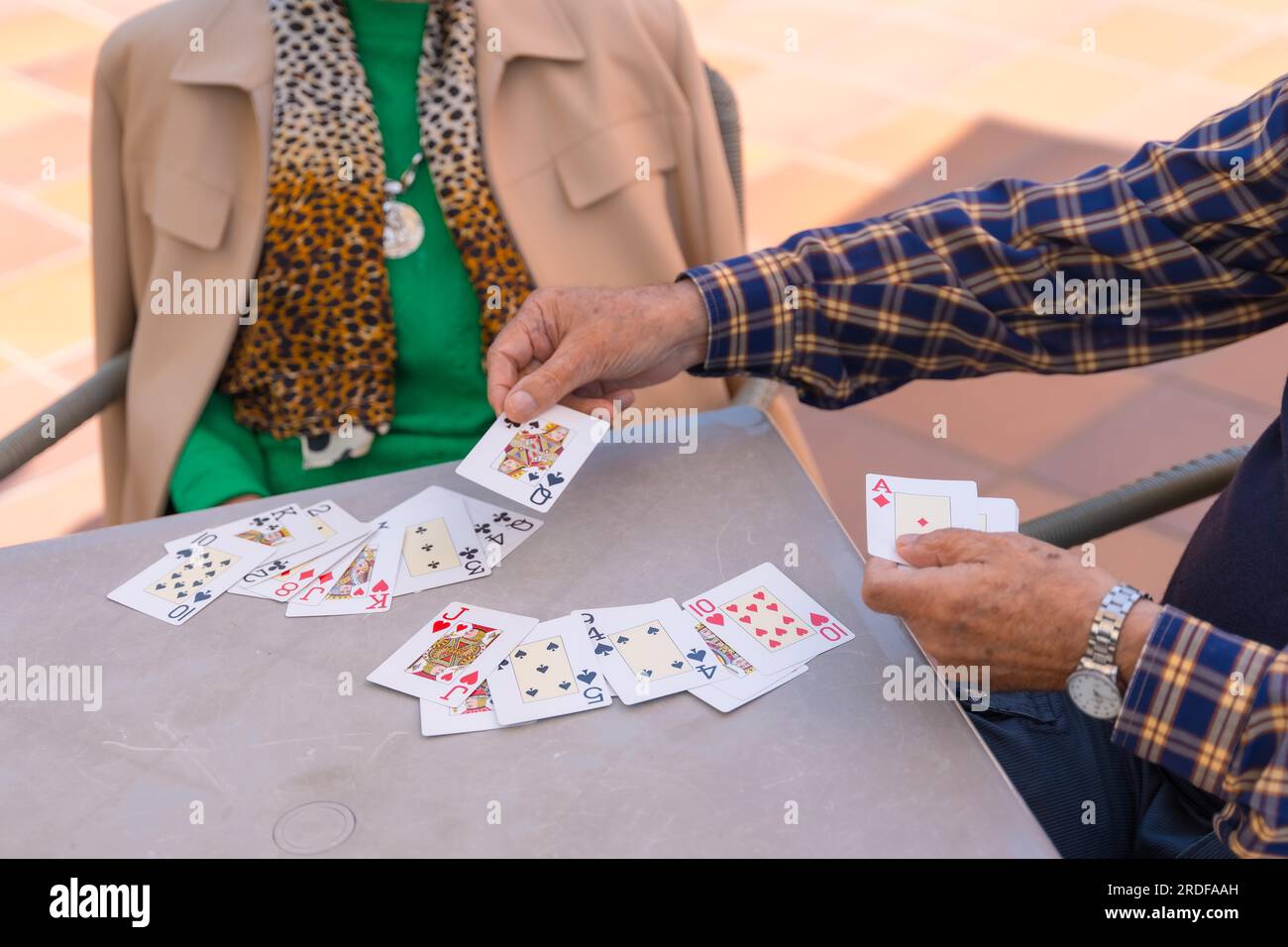 Hands of two elderly people in the garden of a nursing home or retirement home playing cards on a summer morning Stock Photo