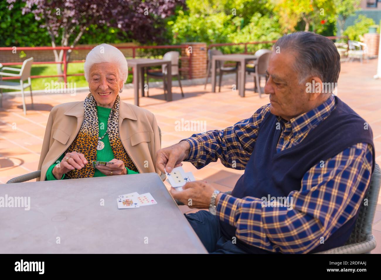Two elderly people in the garden of a nursing home or retirement home playing cards on a summer morning Stock Photo