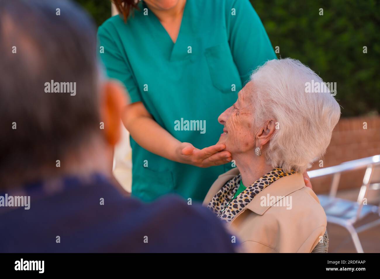 An older or mature woman with the nurse in the garden of a nursing home in a moment of love and affection caressing the face Stock Photo