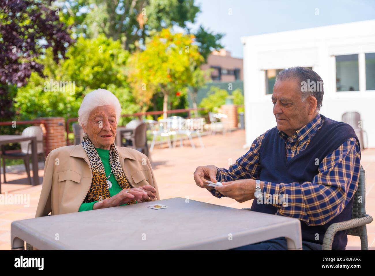 Two elderly people in the garden of a nursing home or retirement home playing cards on a summer morning Stock Photo