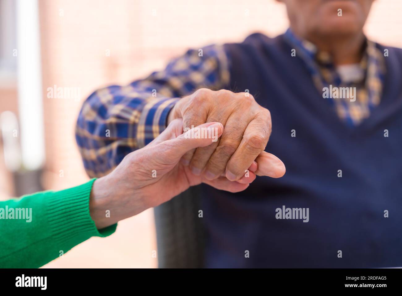 Detail of the hands of two elderly people in the garden of a nursing home or retirement home holding hands in a moment of affection Stock Photo
