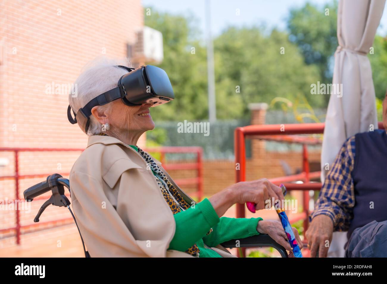 An elderly woman with the nurse looking through virtual reality glasses in the garden of a nursing home, vr glasses Stock Photo