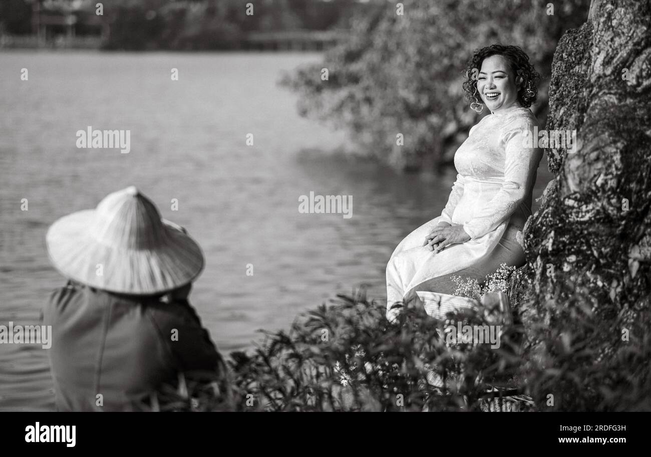 A middle aged Vietnamese woman wearing a traditional 'Ao Dai' poses for a photograph next to Hoan Kiem Lake in central Hanoi, Vietnam. Stock Photo