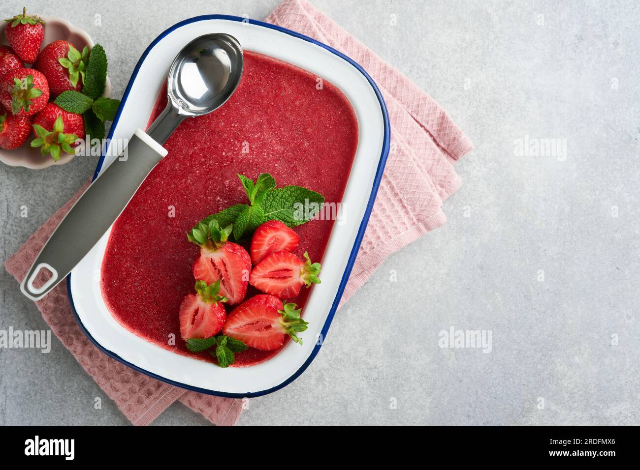 Strawberry granita or fresh berry sorbet in white rustic bowl on gray concrete background. Ice cream with strawberry and mint. Summer treat. Top view. Stock Photo